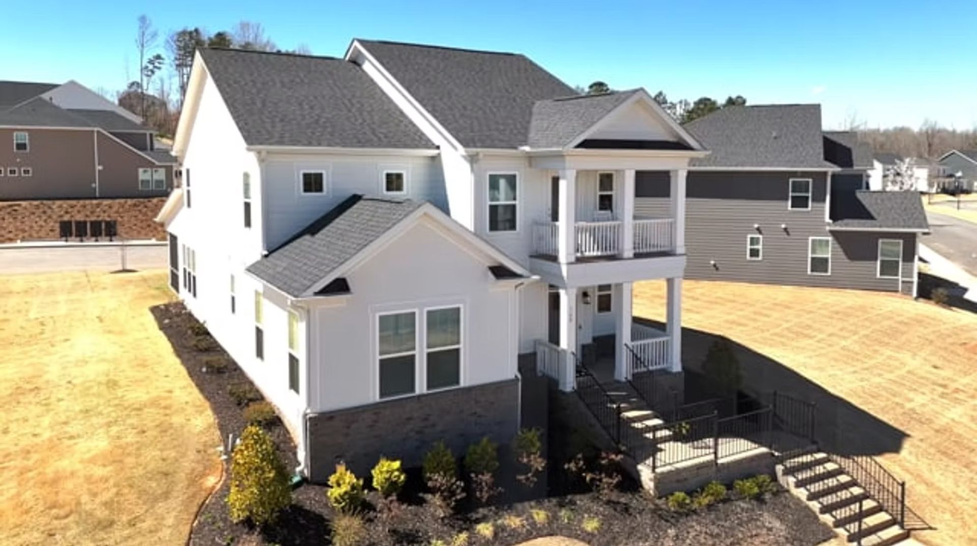 Suburban two-story white house with gray roof, front porch, and a small lawn in a residential neighborhood