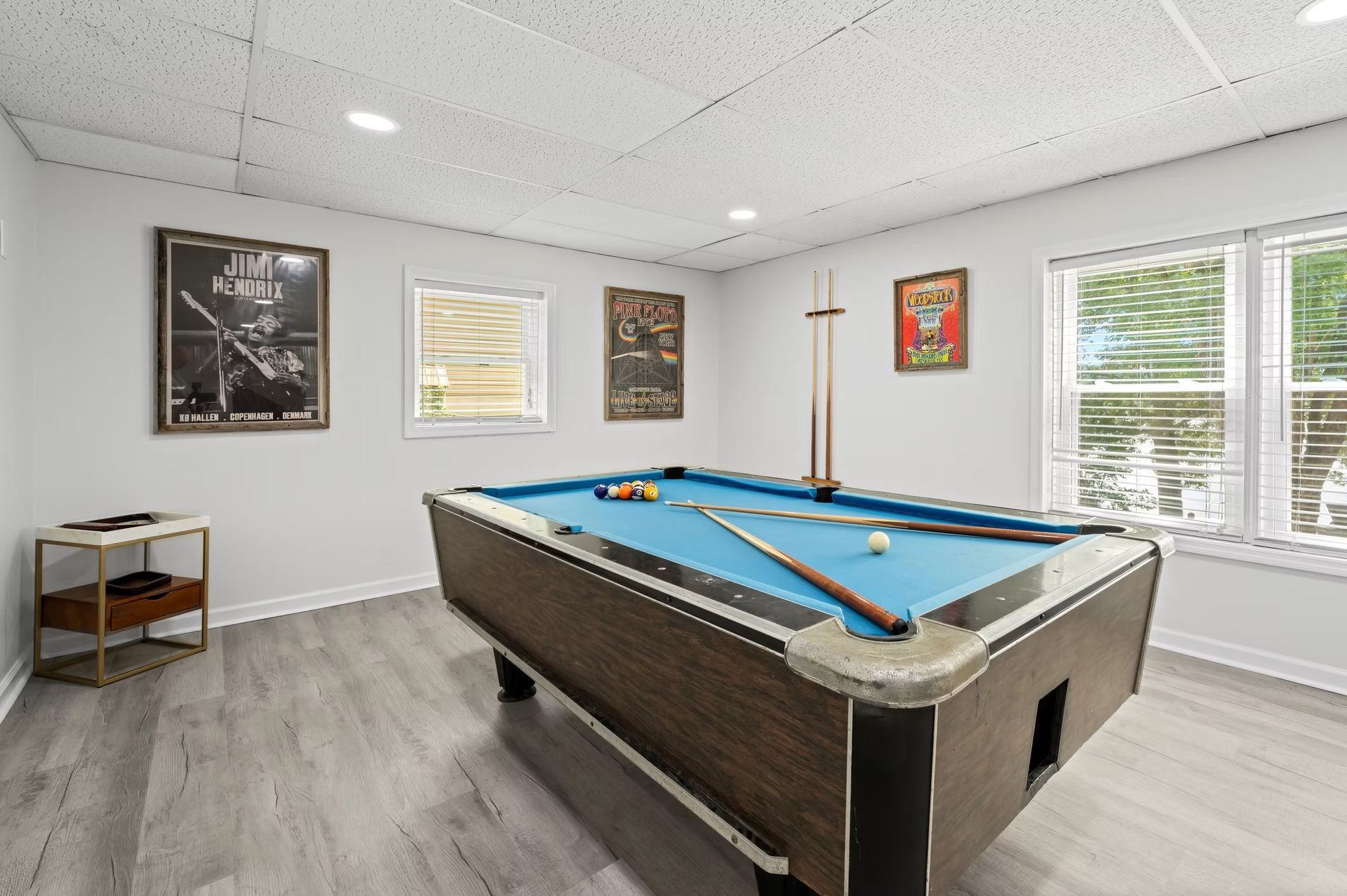Bright game room with a pool table, wall art, and windows with white blinds.