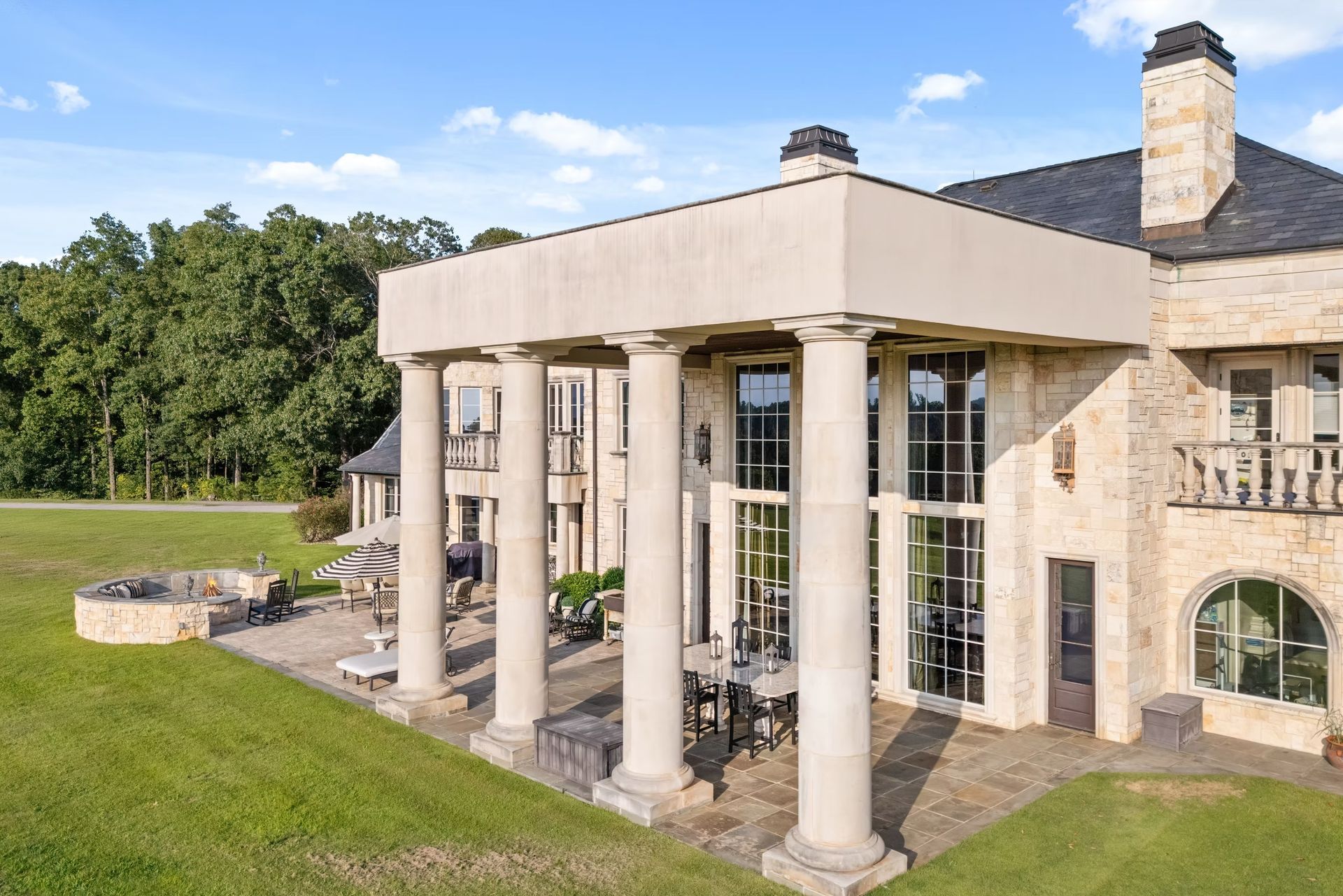 Luxury stone mansion with large white columns and a manicured lawn under a blue sky