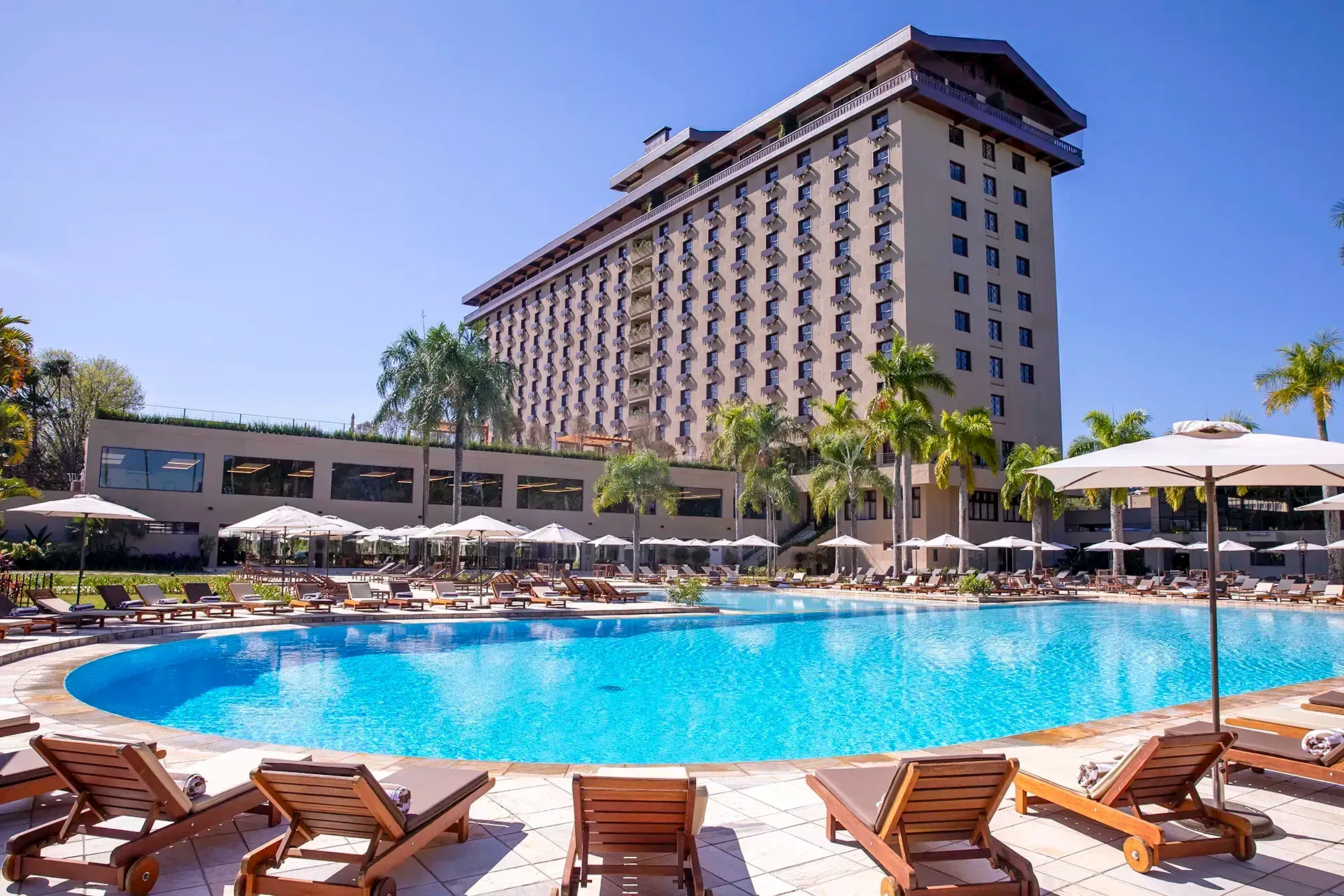 Uma grande piscina cercada por cadeiras e guarda-sóis em frente a um hotel.