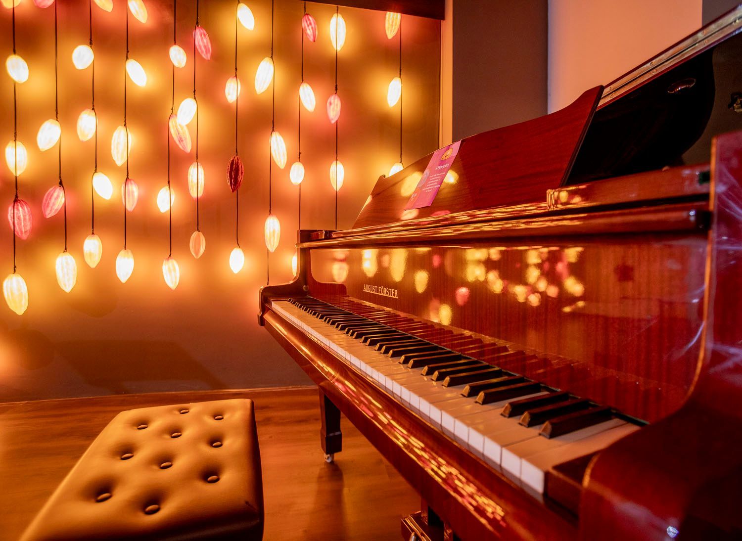 Um piano de cauda vermelho está em uma sala com luzes de natal penduradas no teto.