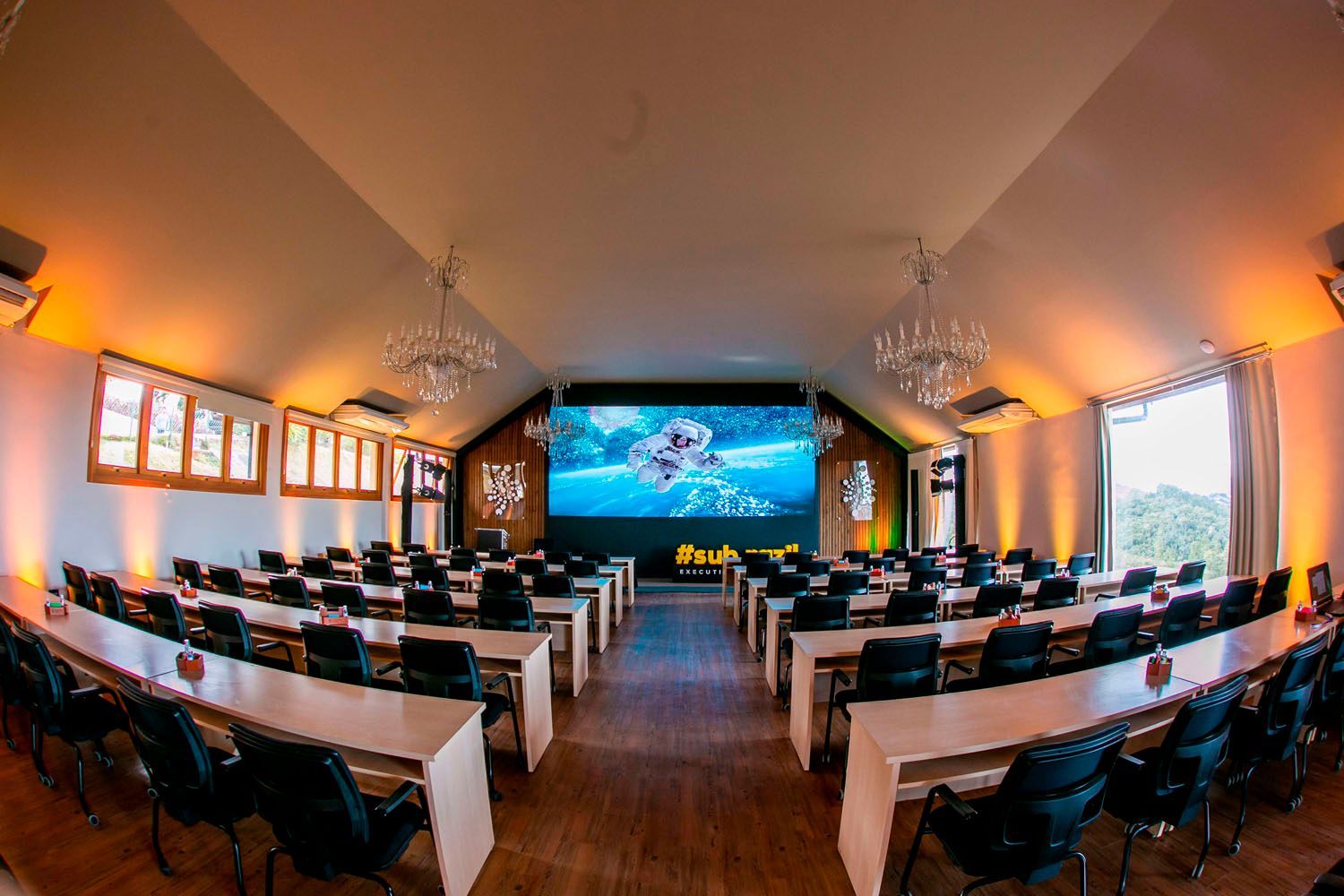 Uma grande sala de conferências com mesas e cadeiras e uma tela grande.