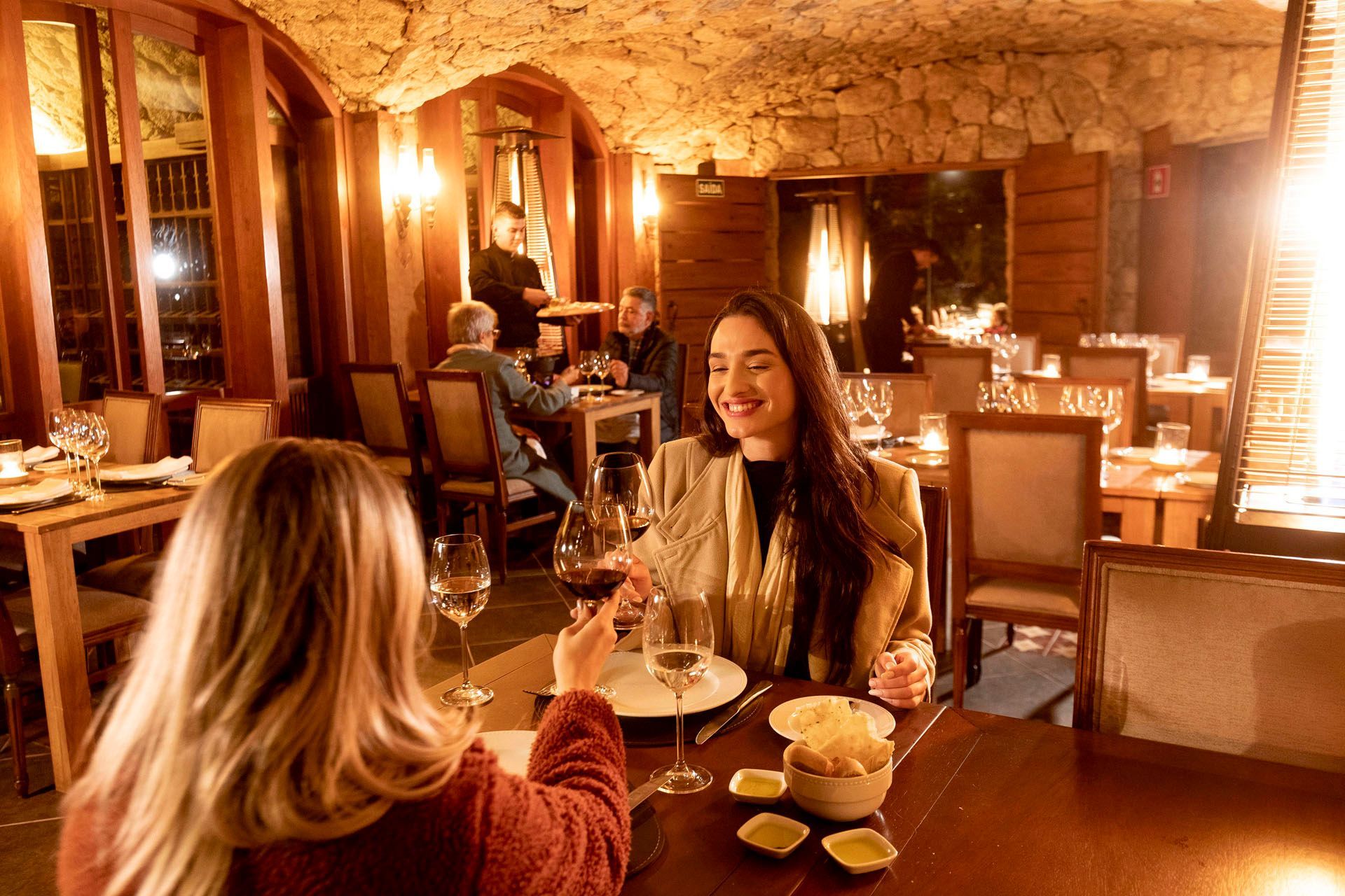Duas mulheres estão sentadas à mesa de um restaurante bebendo vinho.