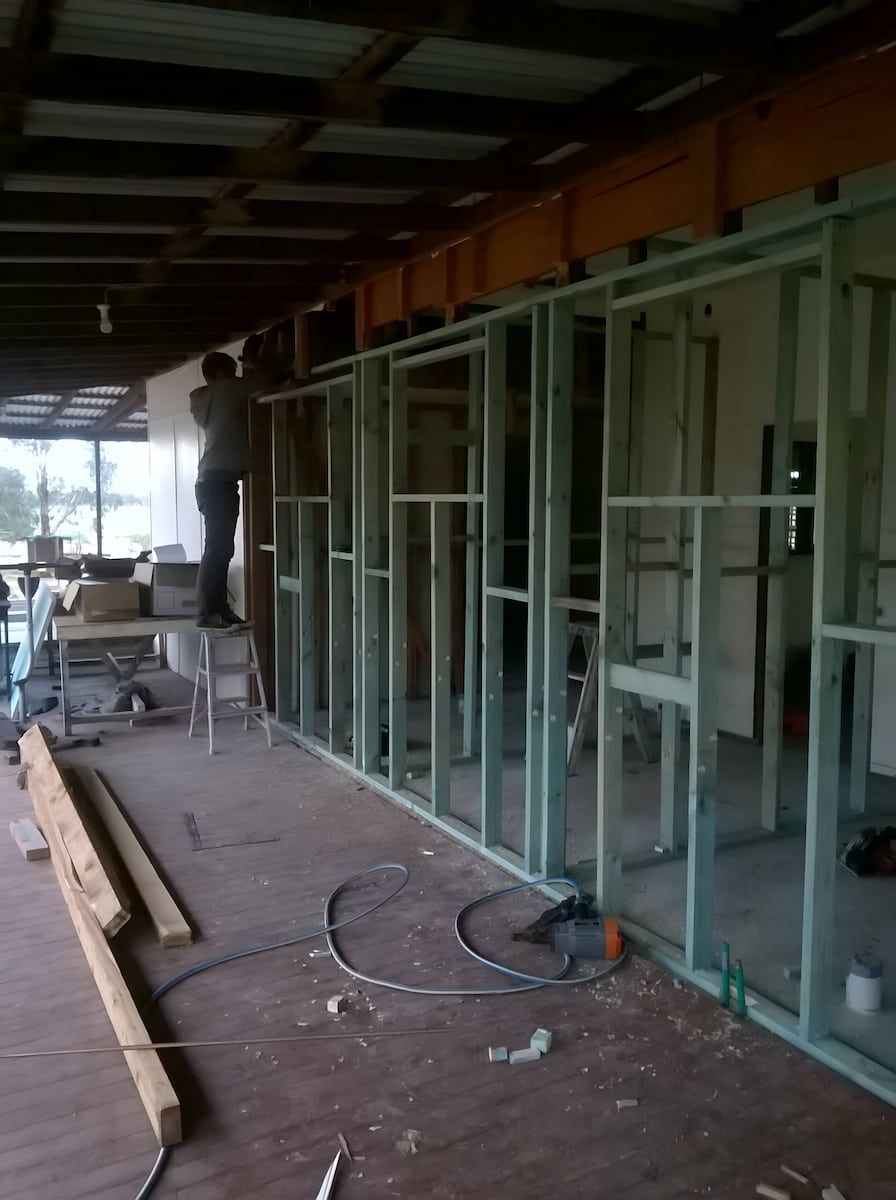 A Person Stands on a Ladder Working on the Framing of a New Interior Wall — Daniher Building Company in Flynn, ACT