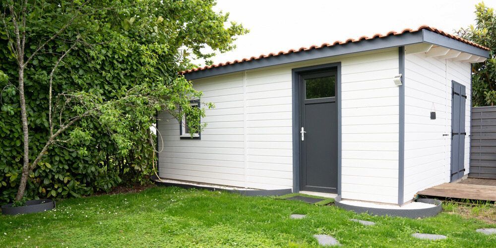 A Small, White Wooden Shed With Grey Trim and Doors Stands — Daniher Building Company in Flynn, ACT