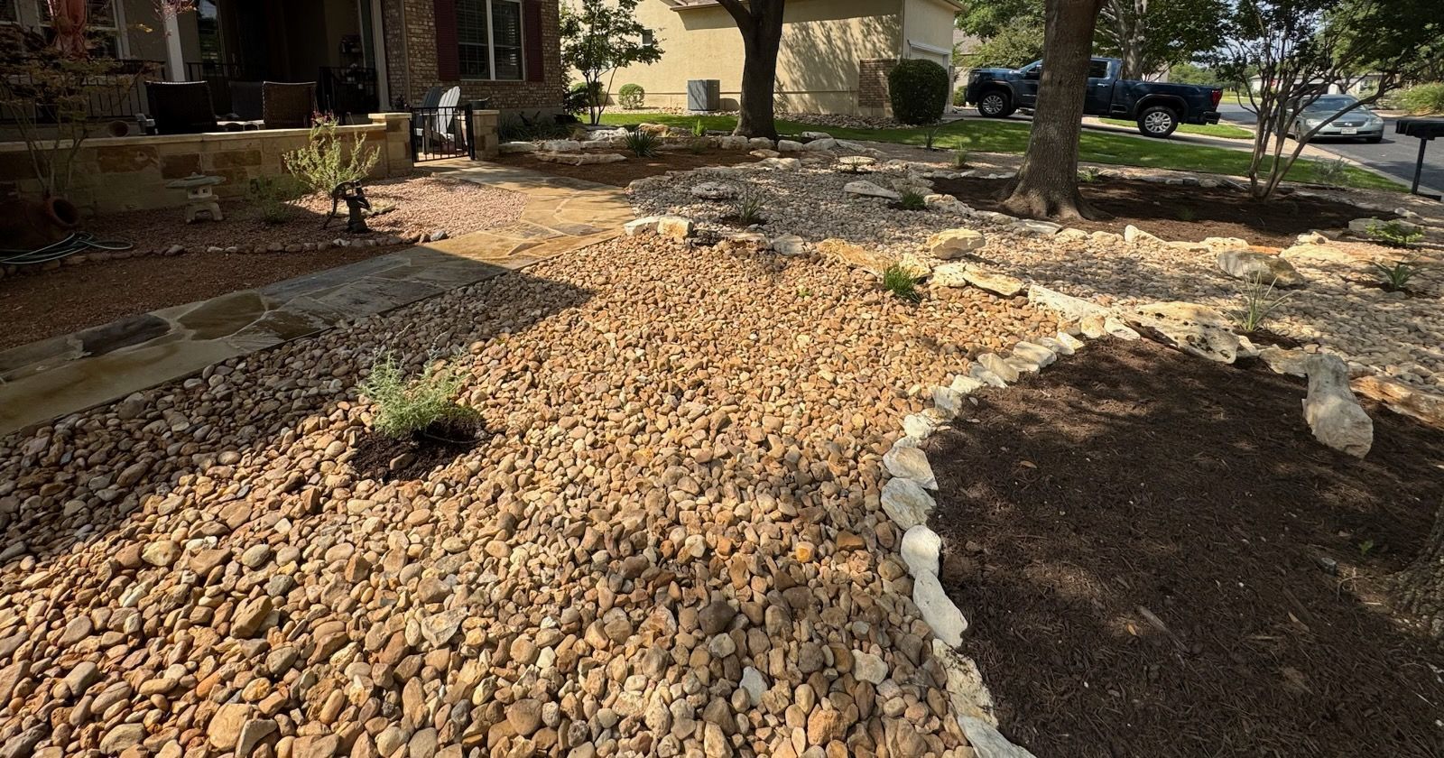 Landscaped front yard with various plants, rocks, and borders in front of a house.