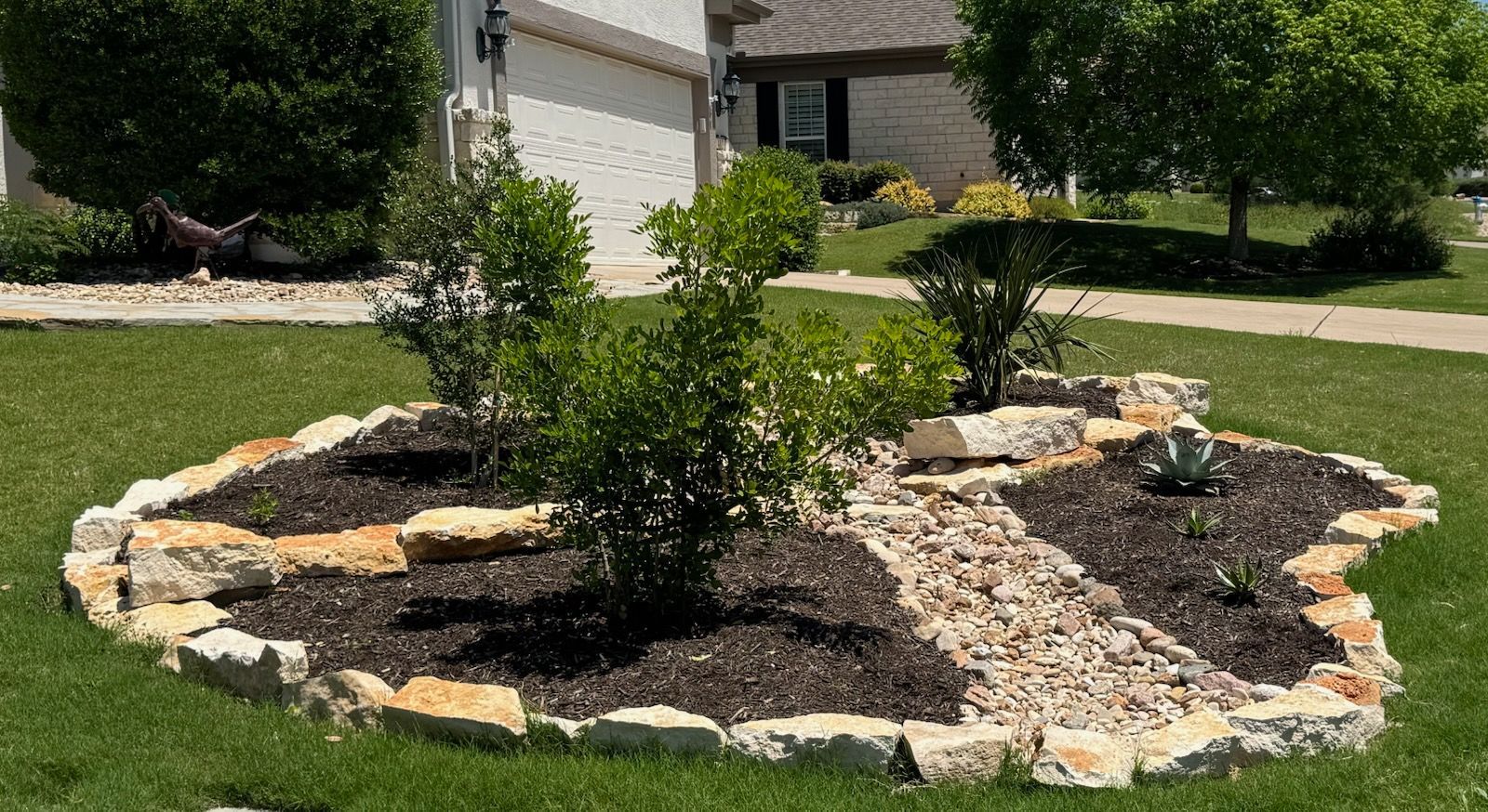 Landscaped front yards with gravel, plants, and small trees along a sidewalk in front of houses.