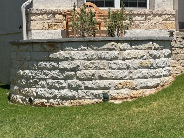 Low stone retaining wall with a bench and greenery against a light-colored house.