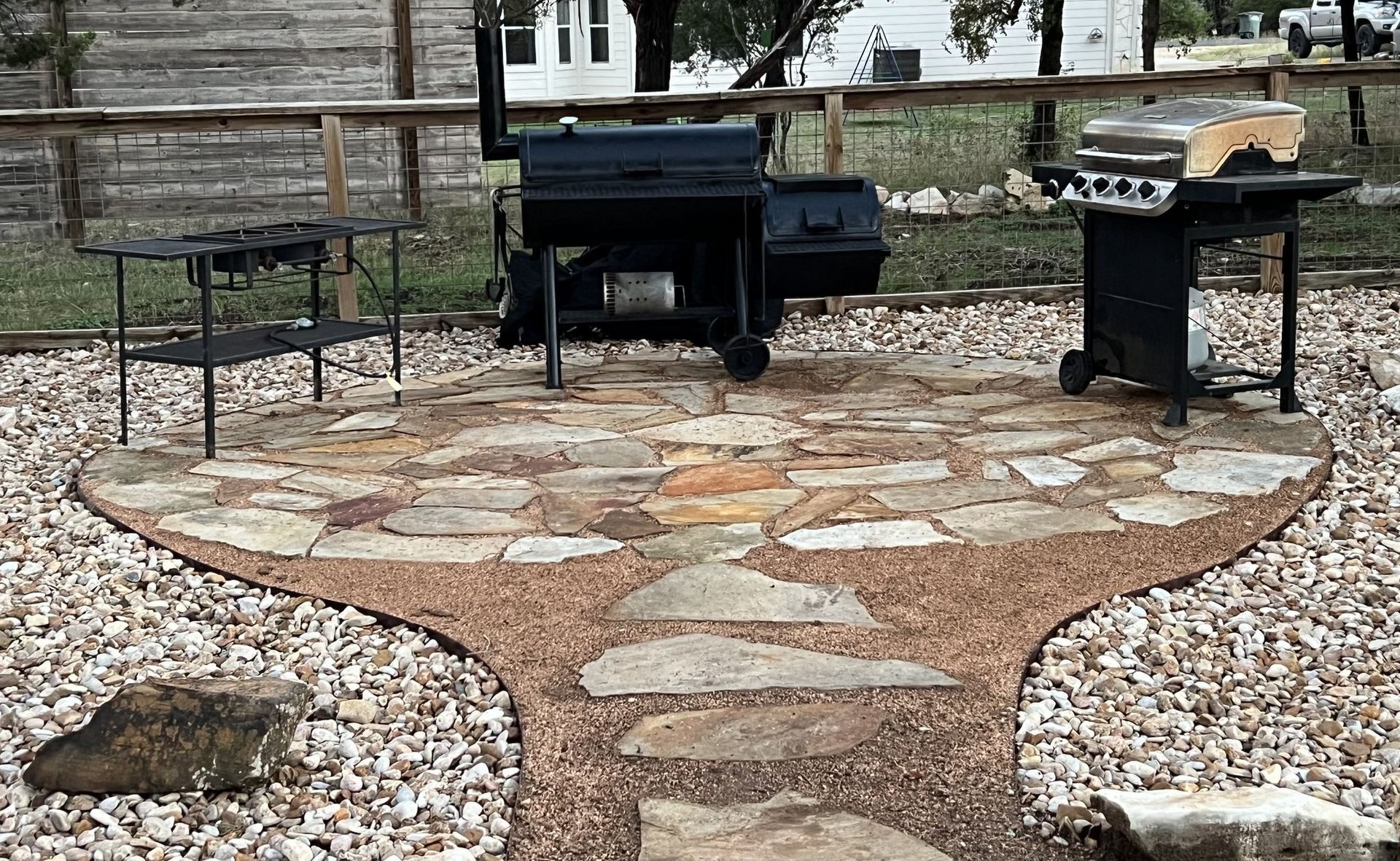 Patio with stone pavers, gravel path, and three grills.