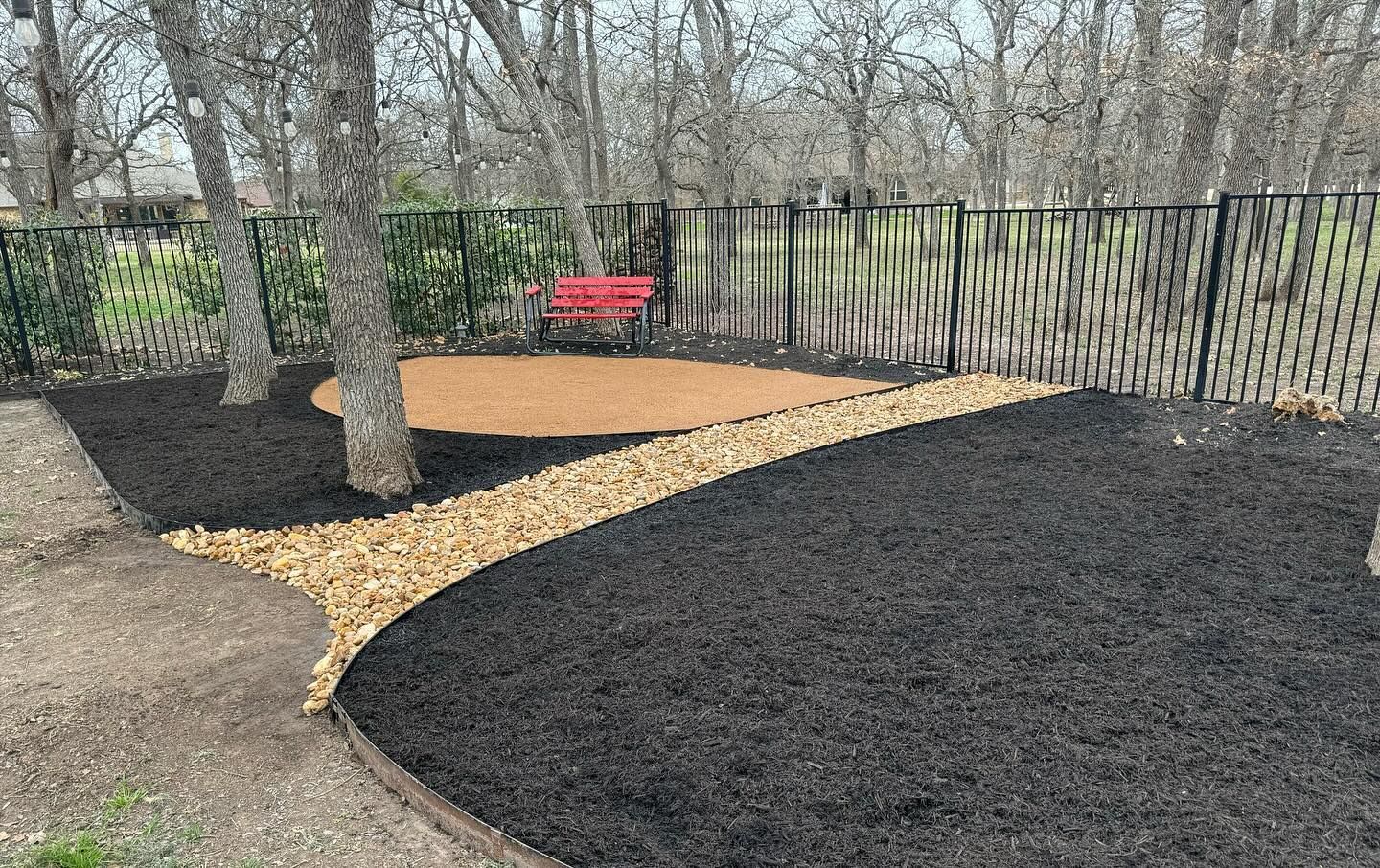 Backyard with black mulch, a rock path, a red bench, and a black fence.