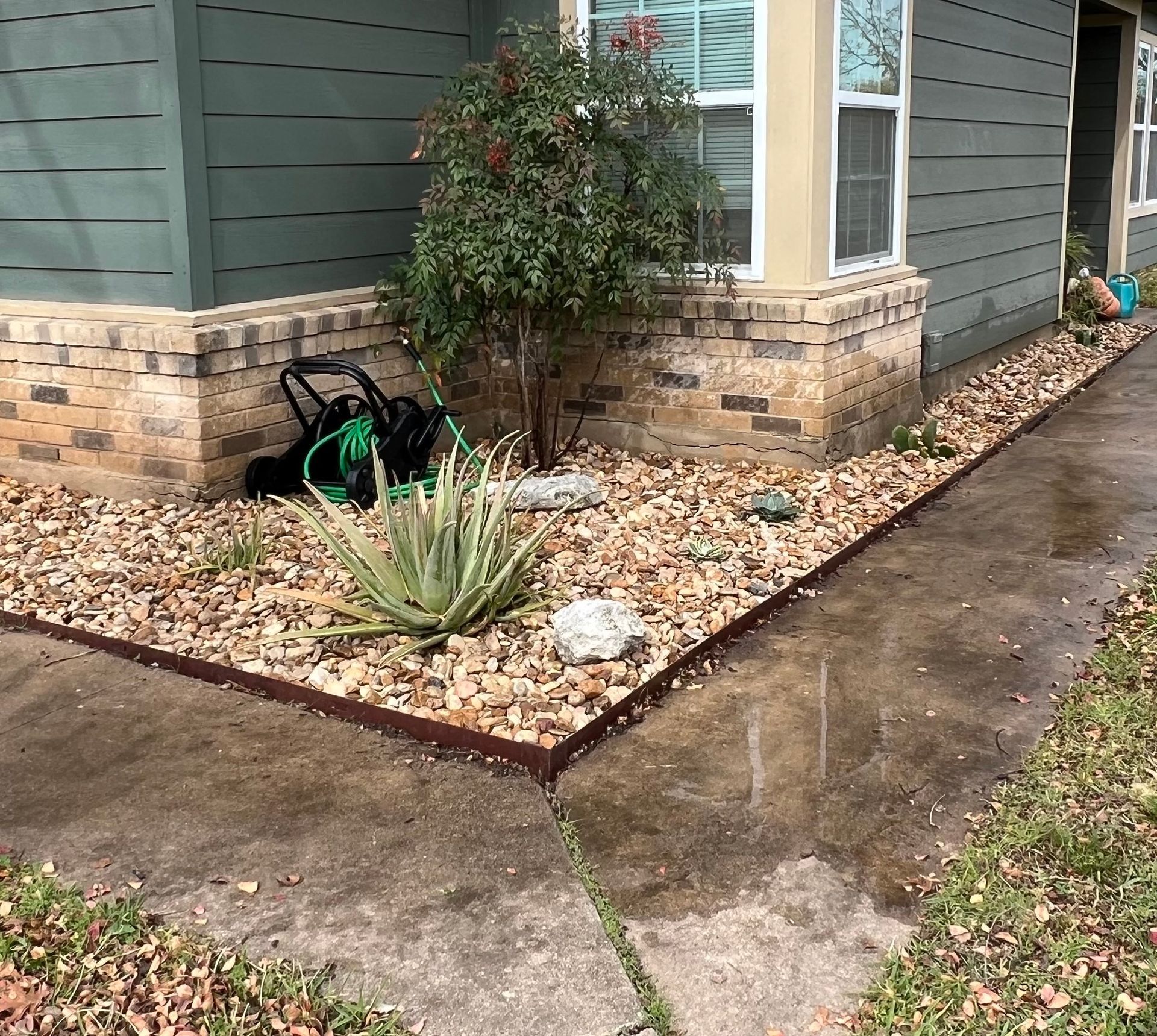 A house exterior with a landscaped border filled with rocks and plants. A sidewalk runs alongside.