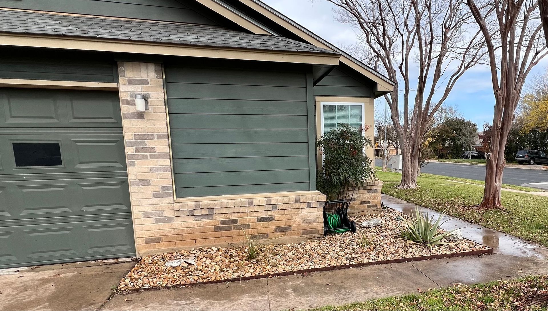 Green house with brick accents, brown gravel, and a sidewalk.
