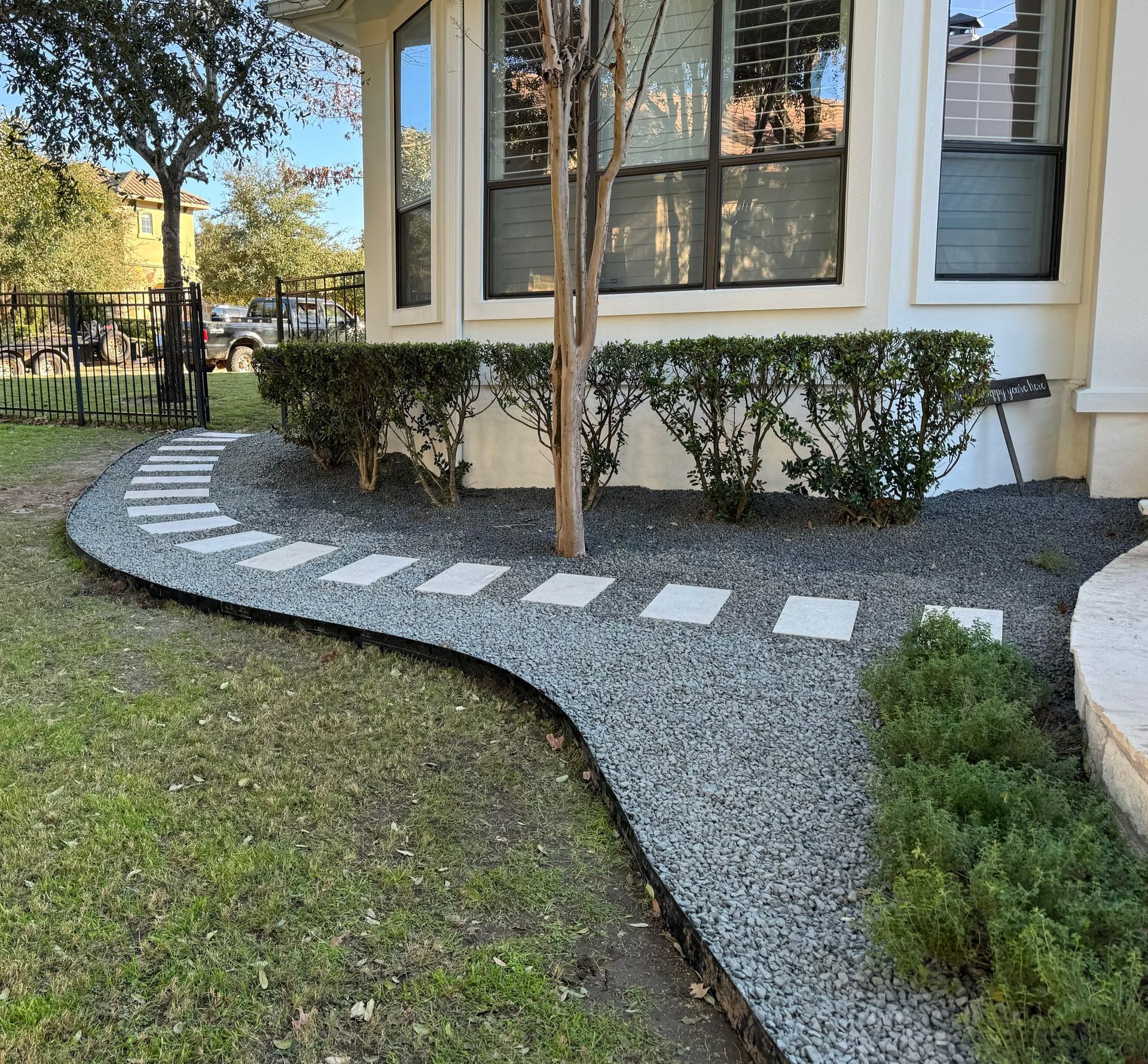 Pathway of stepping stones and gravel leads to a house with shrubs and a tree.