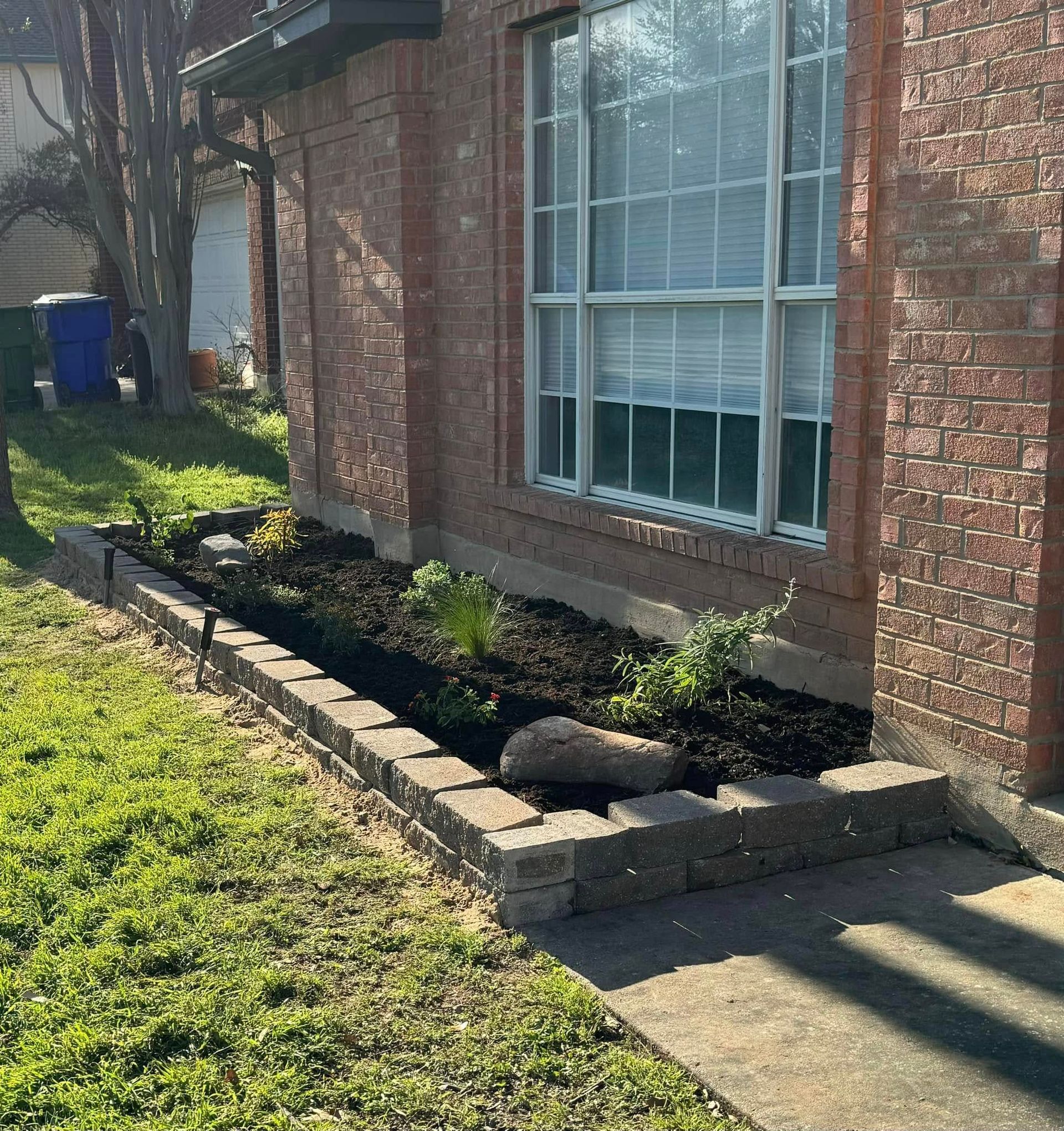 Brick house with a small raised flower bed filled with dark soil and plants.