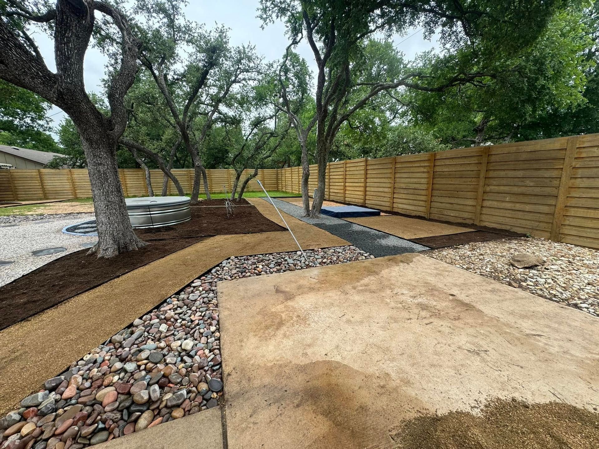 Backyard with gravel paths, mulch, stepping stones, wooden fence, and trees.
