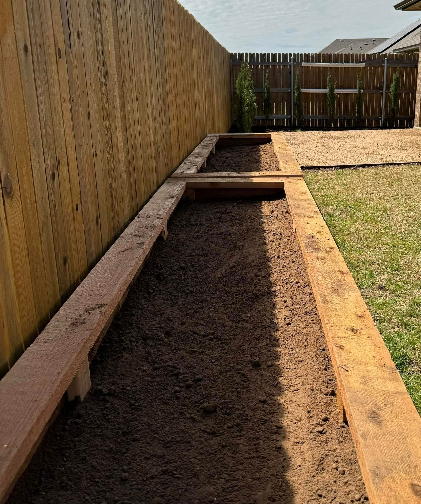 Wooden raised garden beds along a wooden fence, filled with dark soil.