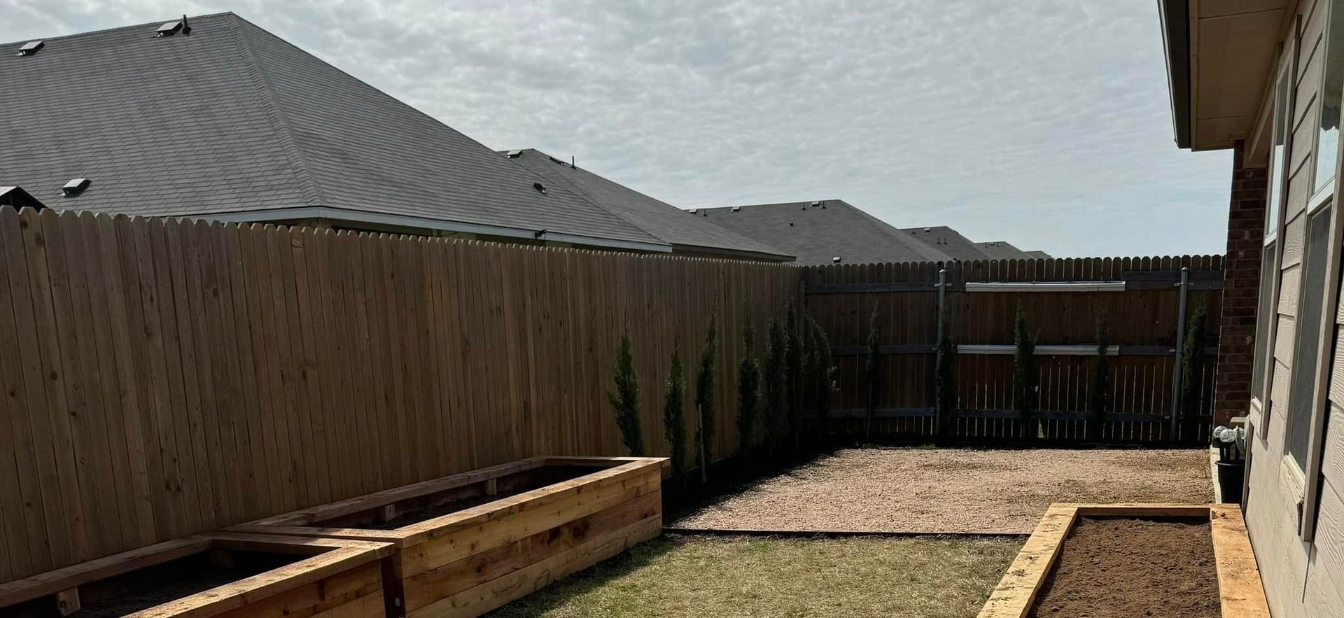 Backyard with wooden fence, raised garden beds, and house siding.
