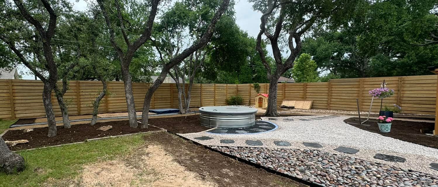 Backyard landscaping with a gravel path, trees, and wooden fence.
