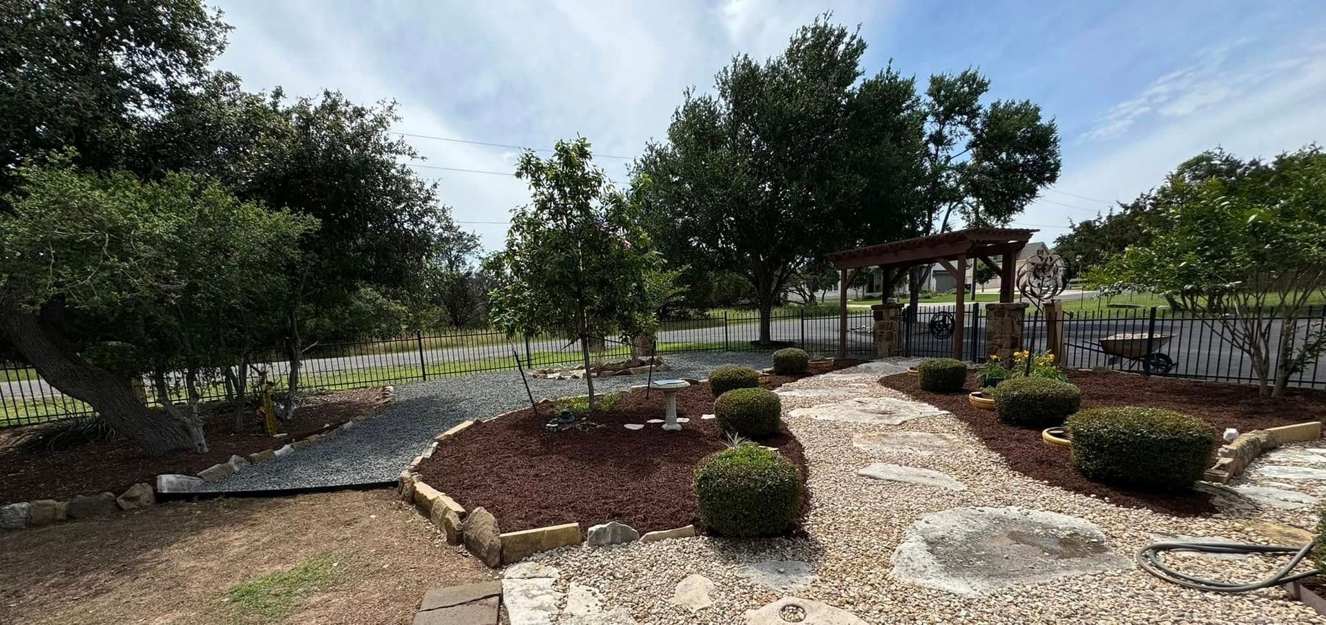 A garden path leads to a wooden structure, trees and a white picket fence on a sunny day.