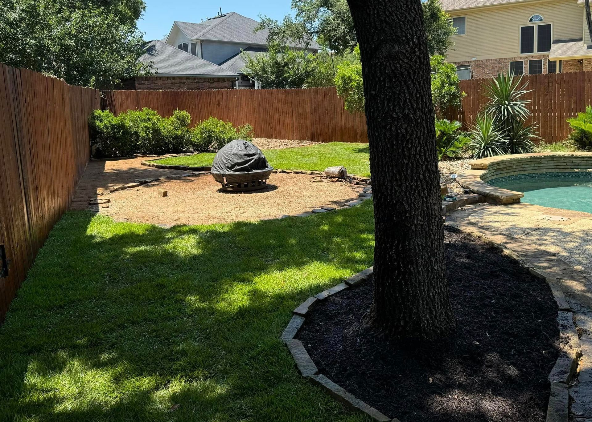 Backyard with a brown fence, green grass, a tree, and a pool.