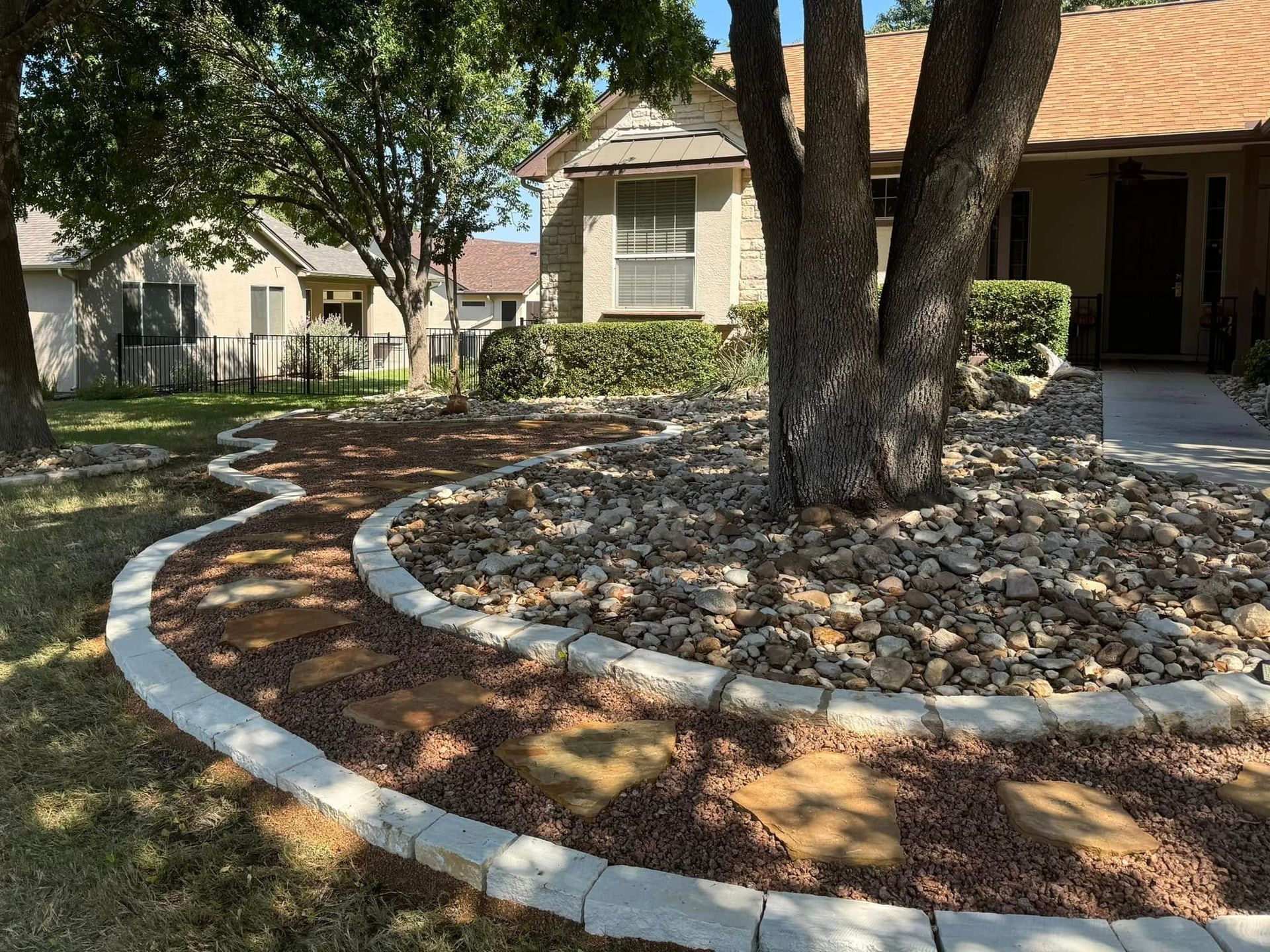 A landscaped front yard with a stone-bordered path and tree surrounded by rocks, leading to a beige house.