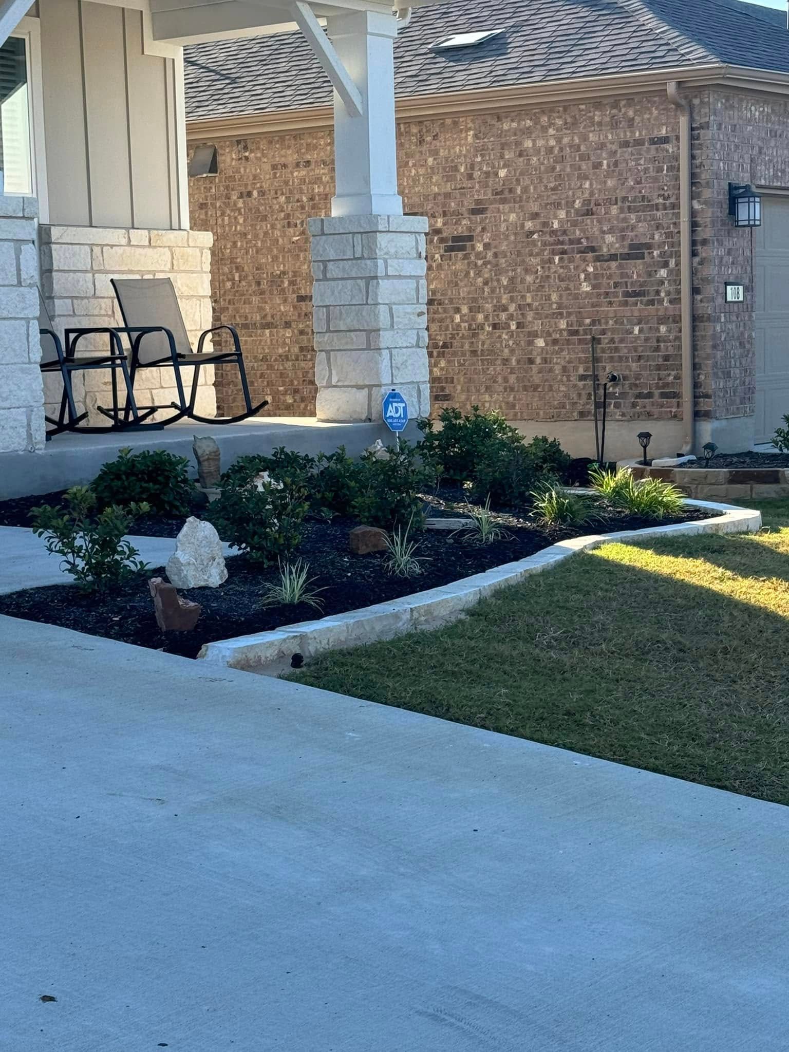 Front yard landscaping with a stone planter bed and porch.