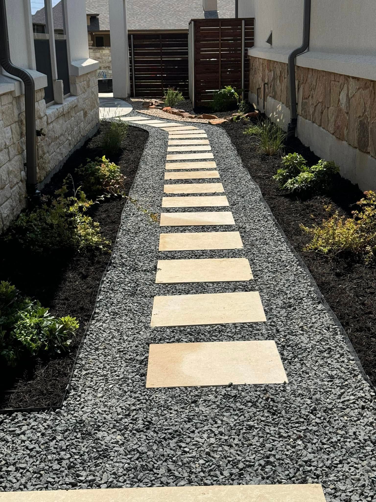 Stone path through a landscaped garden with stepping stones, black gravel, and plants.
