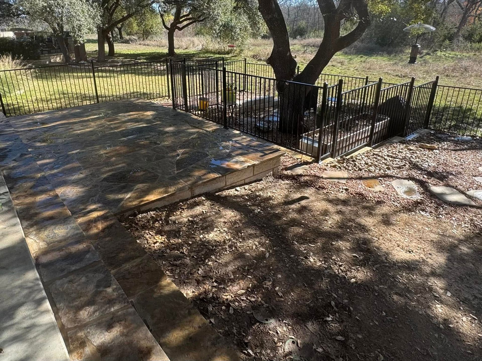 Gravel and stone patio with metal fence around a tree, in a yard.