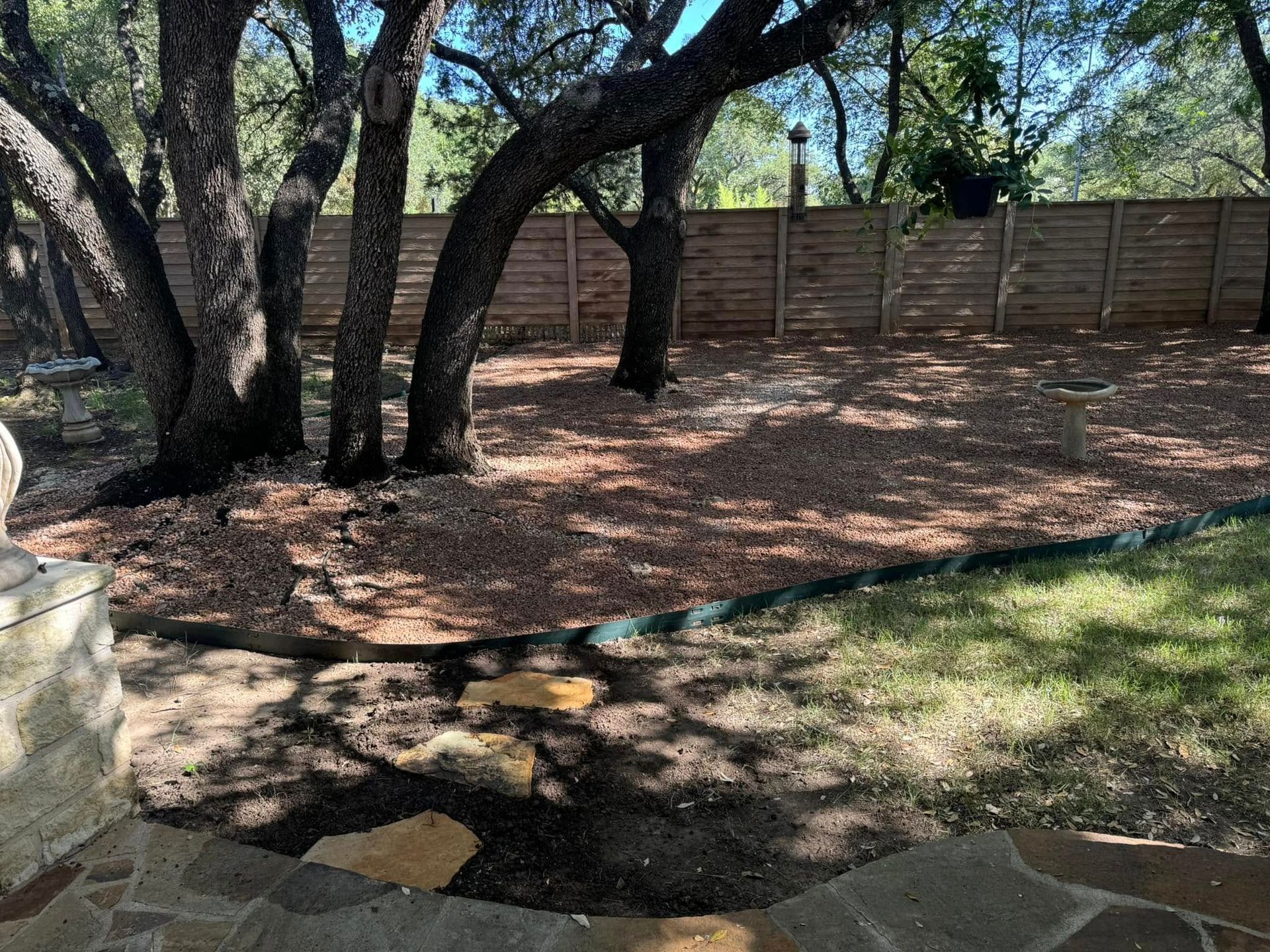 Backyard with trees, gravel, and a wooden fence; stone steps in the foreground lead to the yard.