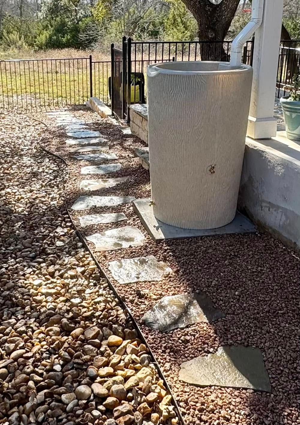 Rain barrel beside a pathway made of stone steps; gravel ground.