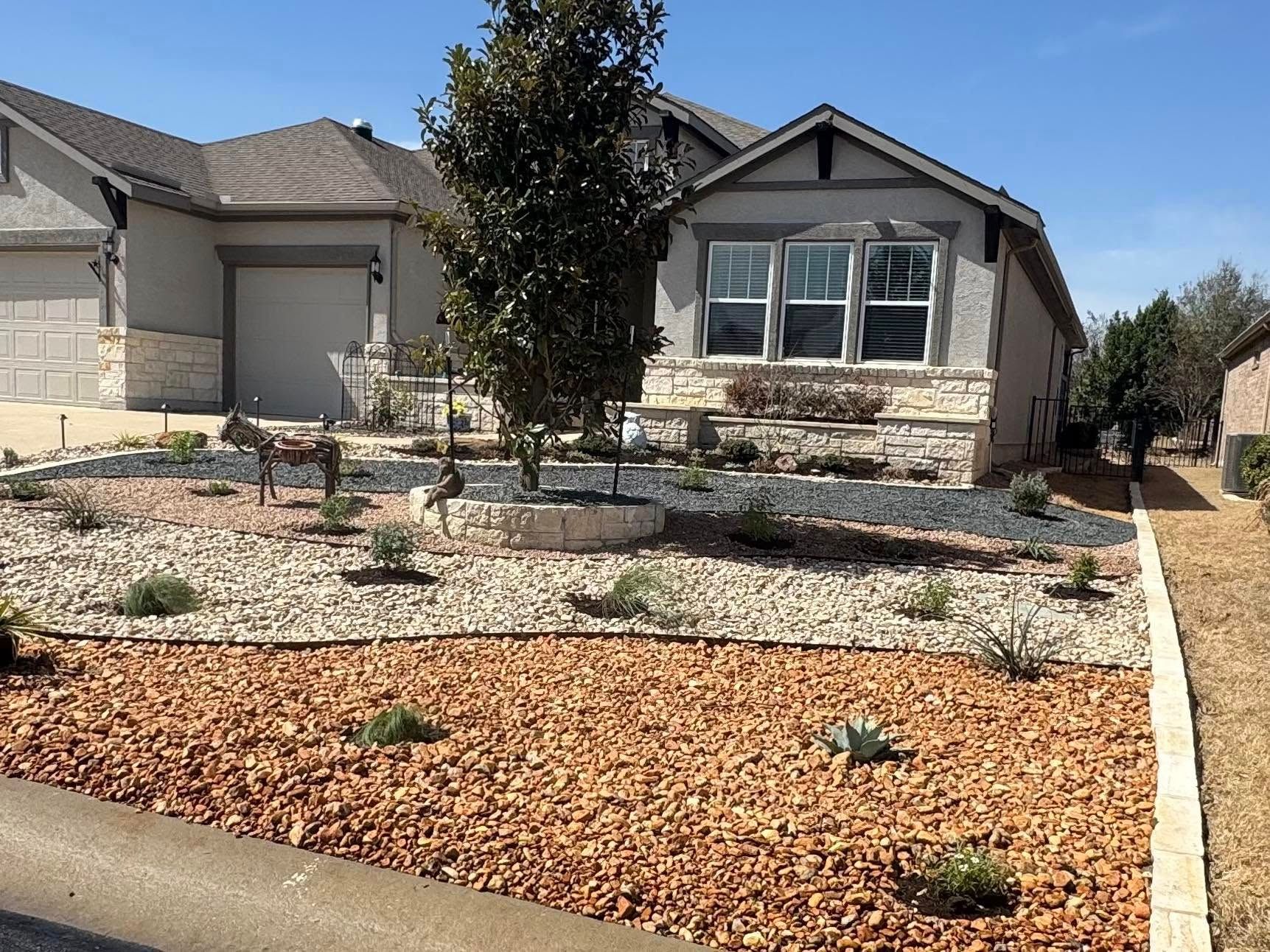 Landscaped front yard with house. Brown and gray stone, tree, and plants.