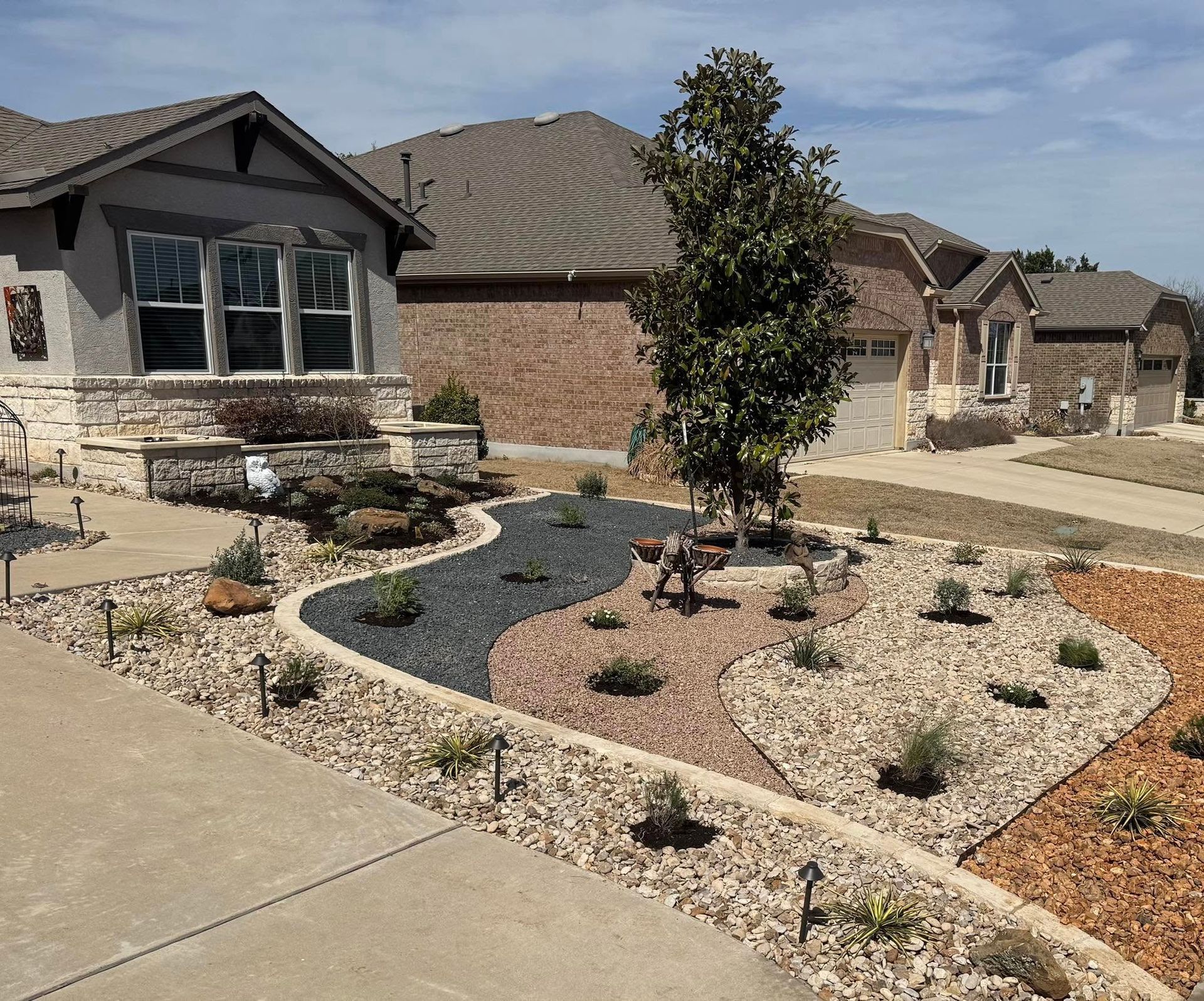 Front yard landscaping with rock beds, a young tree, and a curved walkway leading to a house.