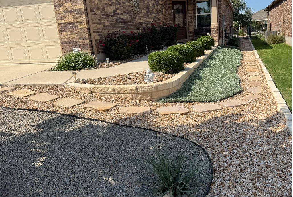 Landscaped front yard with gravel, stone steps, bushes, and a green groundcover in front of a house.