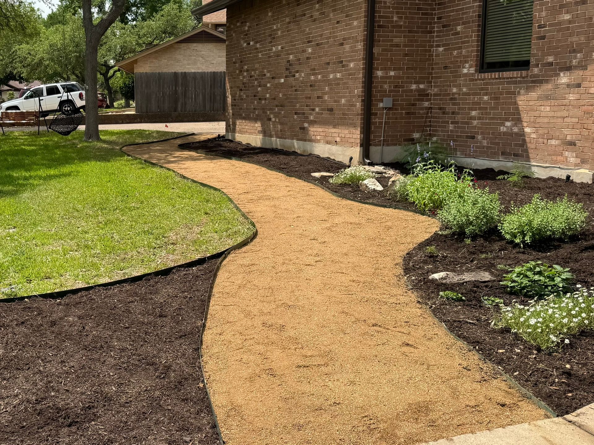 A gravel pathway curves through a yard next to a brick building.