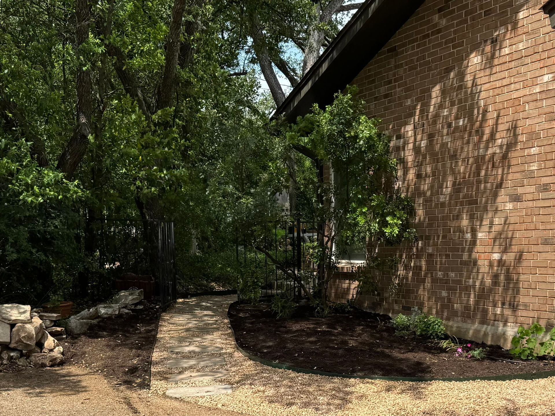 Stone path winds through lush greenery beside a brick building on a sunny day.