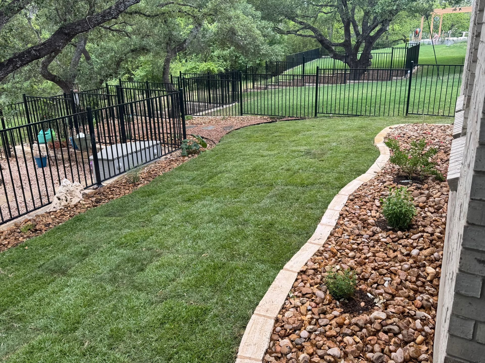 Lawn and rock landscaping with decorative black metal fence and trees.