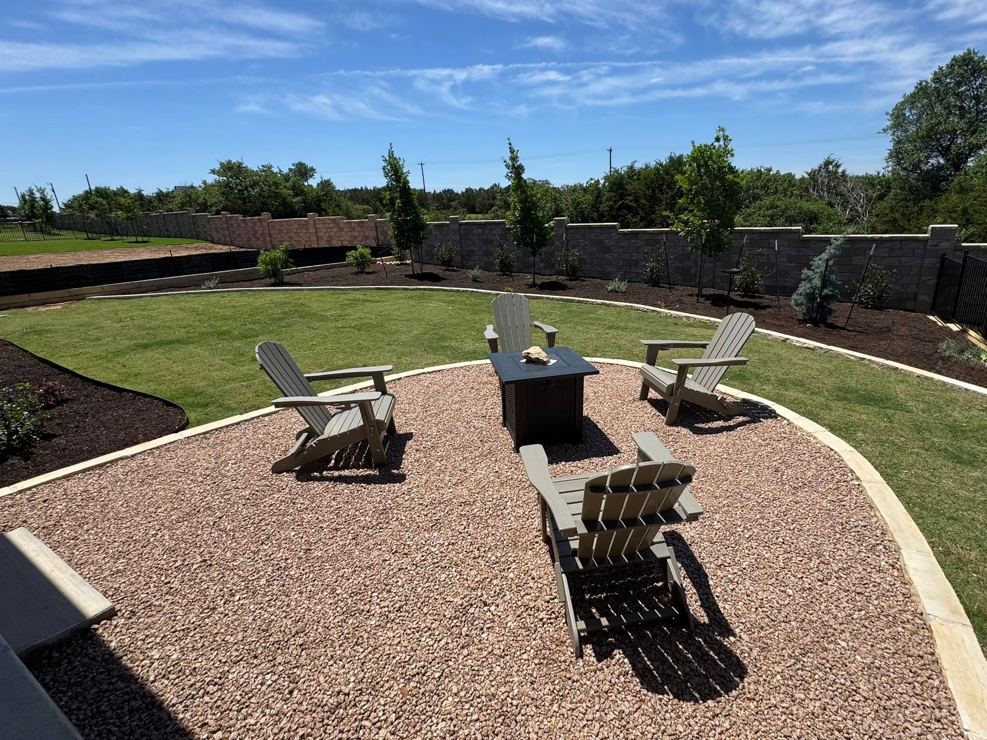 Outdoor seating area with gravel, chairs, fire pit, and a green lawn.