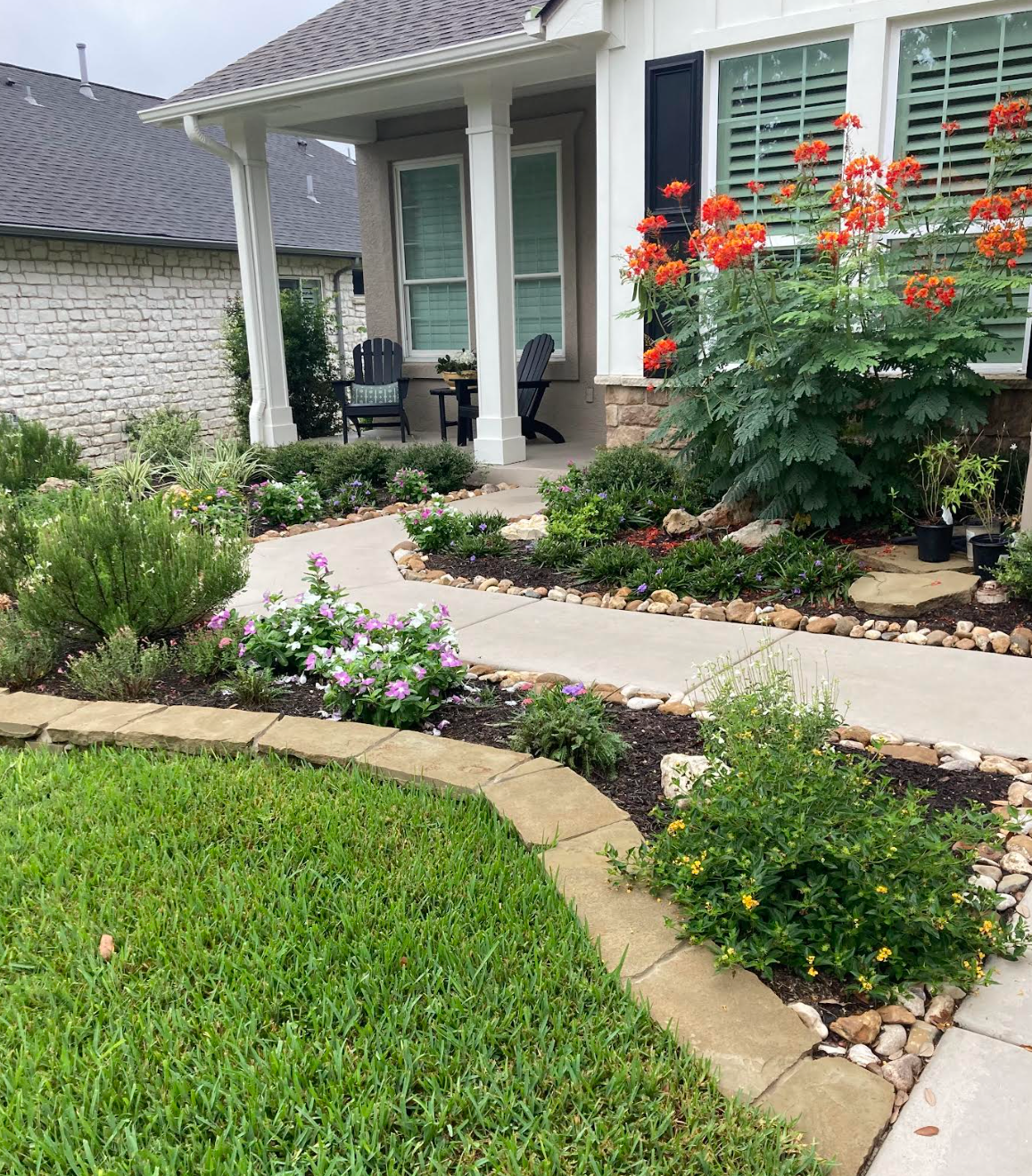 Stone path winding through a landscaped yard with mulch and greenery. Trees and buildings in the background.