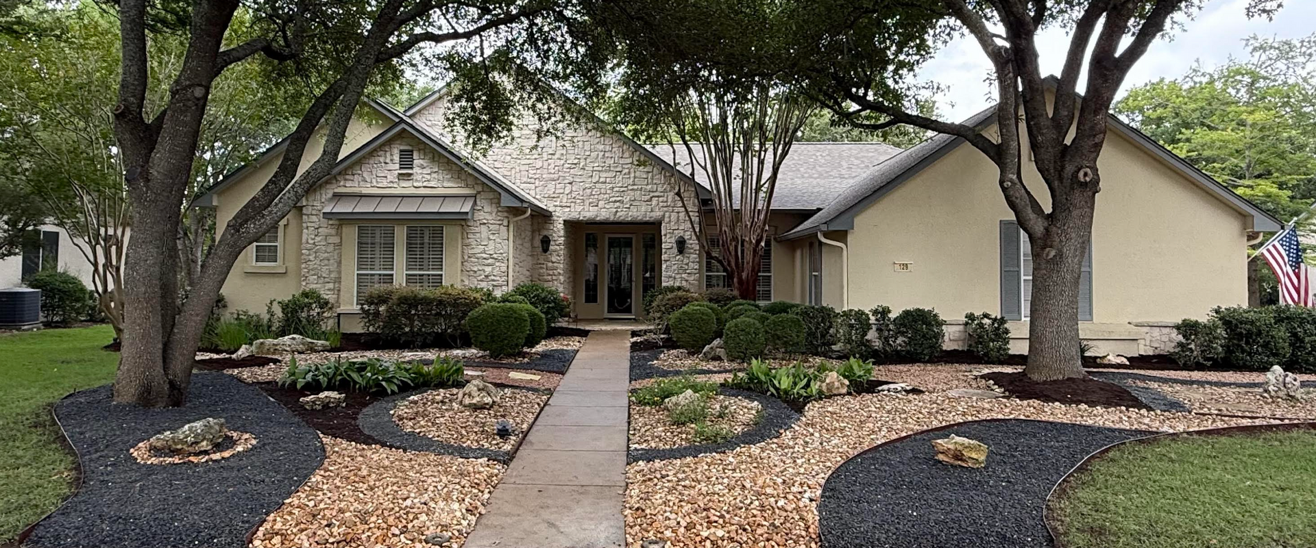 Stone walkway and landscaped front yard with green bushes and gravel.