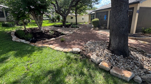 Landscaped backyard with mulch, rocks, a stone border, green grass, and trees.