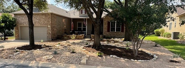 House with stone facade and landscaping. Trees frame the front, driveway in foreground.