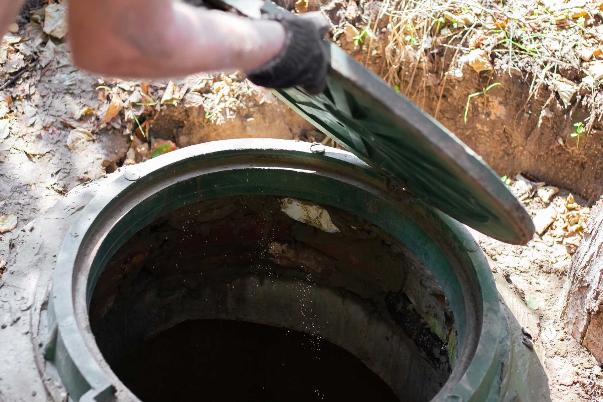 Gloved hands open a septic system tank on the ground to perform professional repair and maintenance.