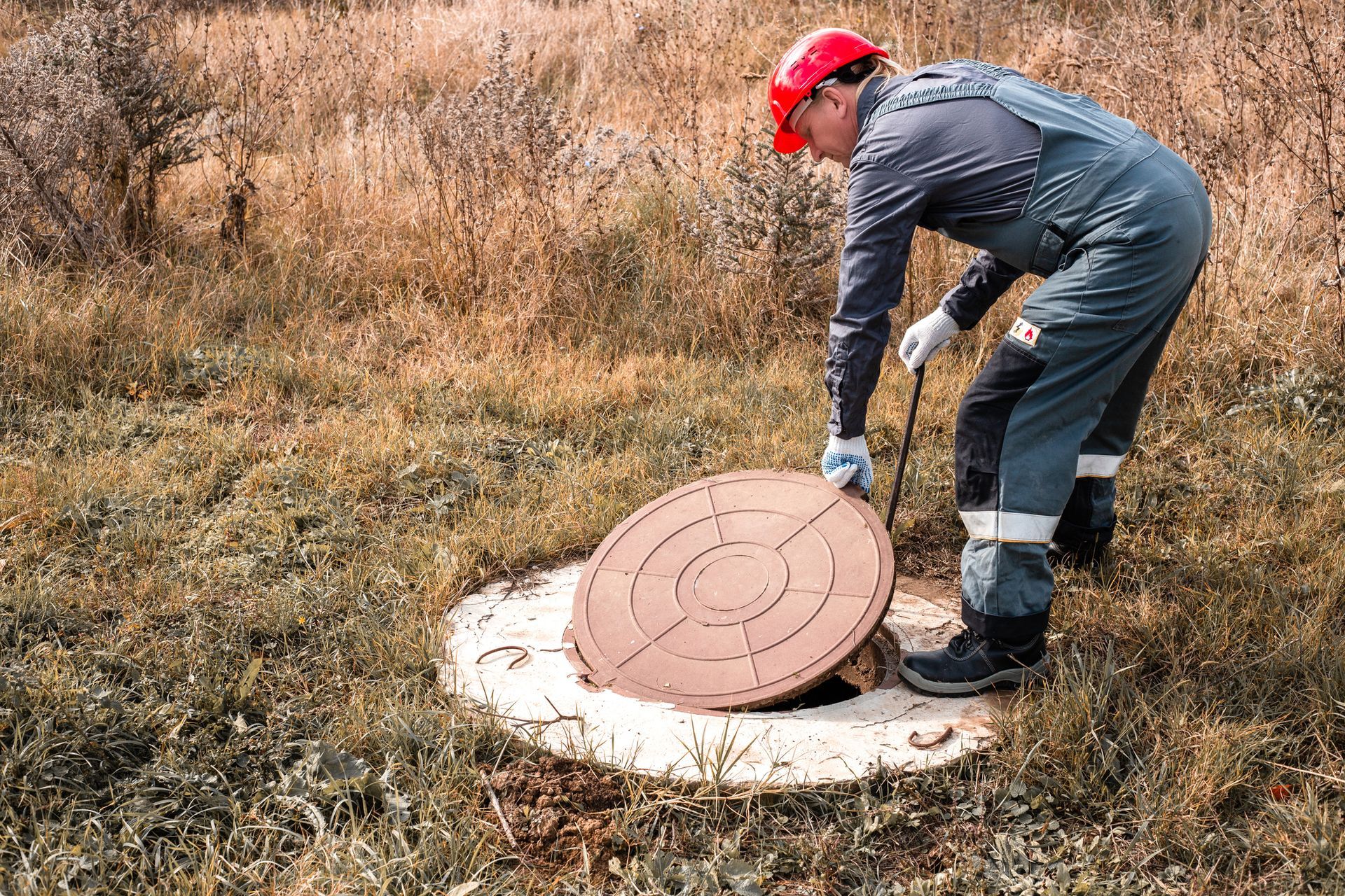 A worker from Madden Septic in a hard hat lifts a manhole cover on a septic system grease trap in Ni