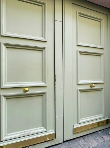 Two light green wooden doors with three rectangular panels, brass handles and a brass kick plate.