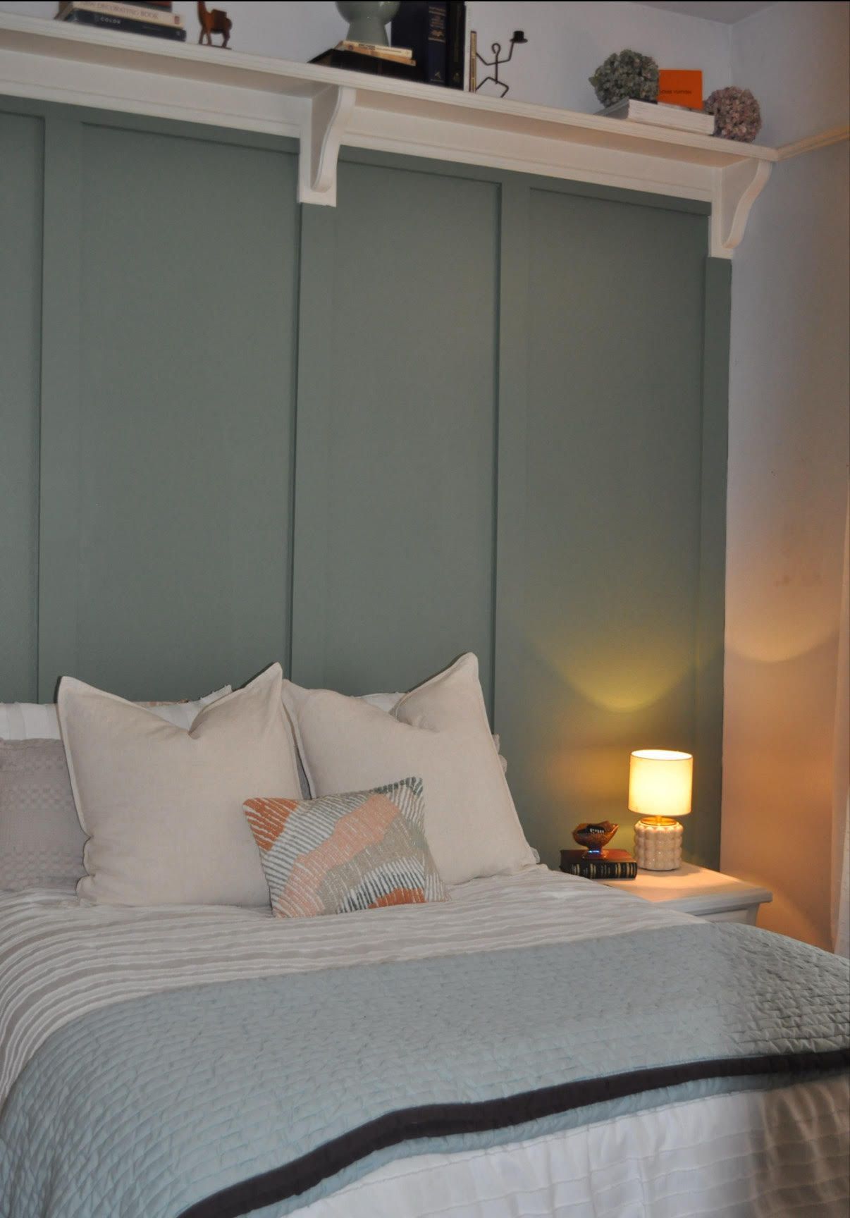 Bedroom with green wall panels, white bedding, and a small table with a lamp.