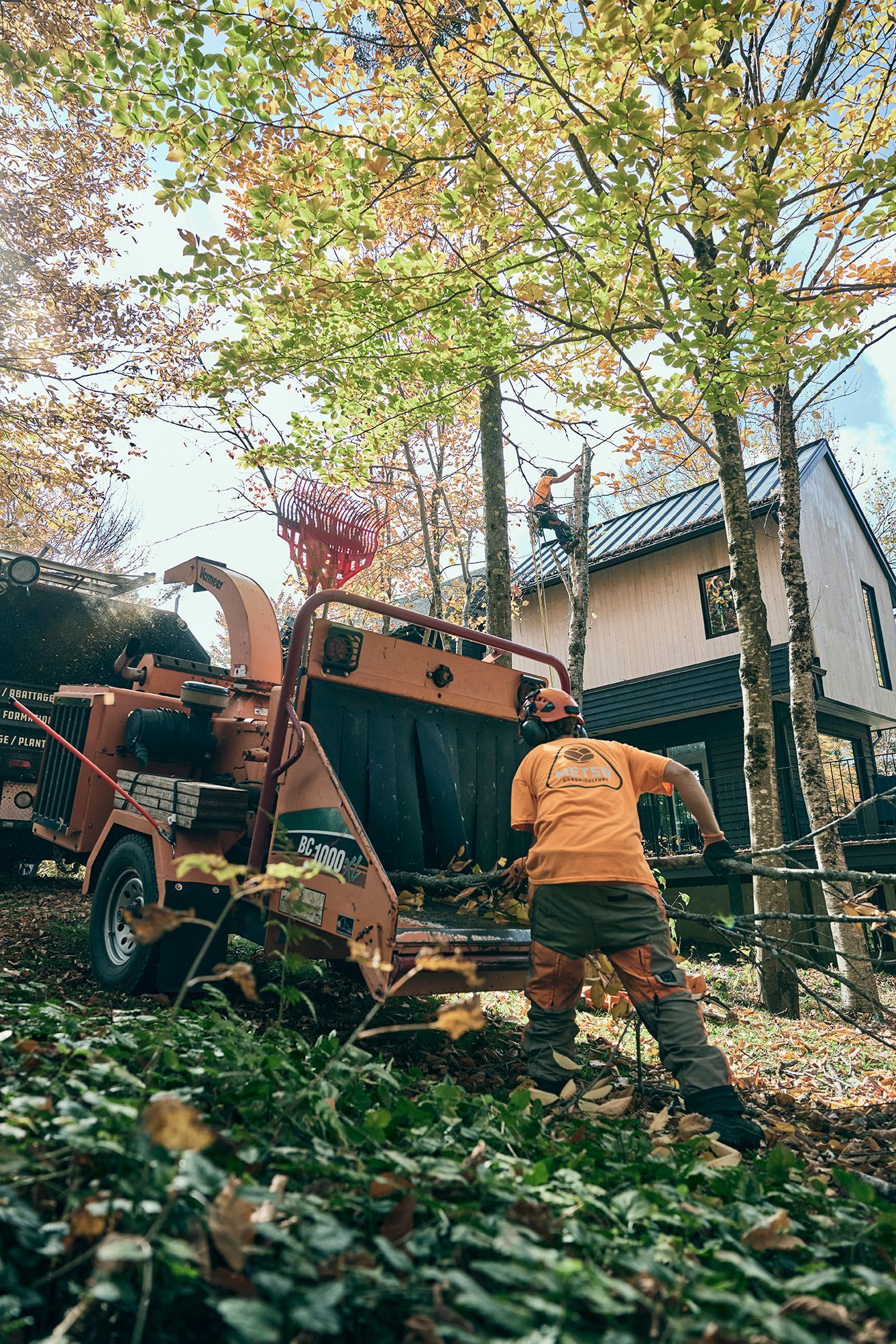 Un homme se tient à côté d'un broyeur d'arbres devant une maison.