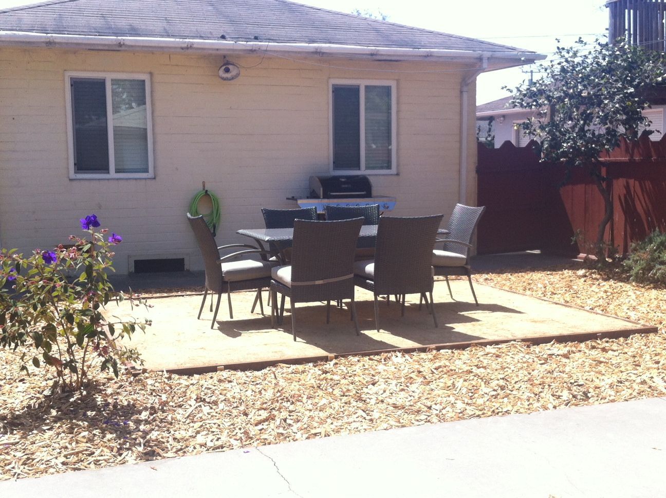 Backyard patio with table, chairs, and grill beside a beige house