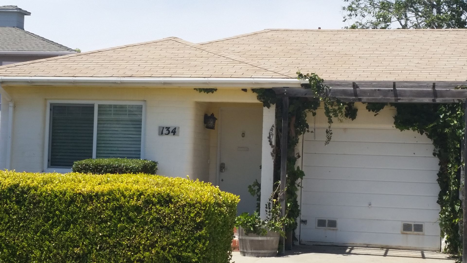 Single-story beige house with a garage, white door, and trimmed hedge in front