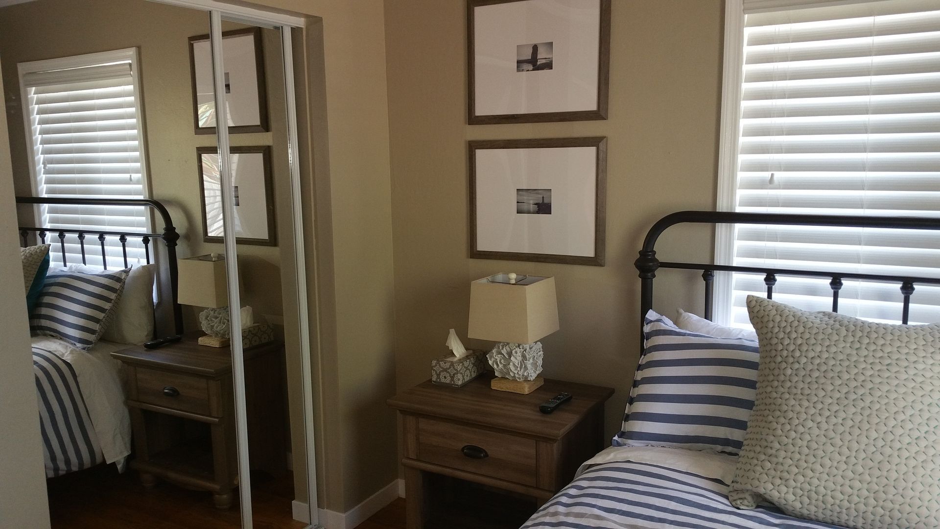 Bedroom with mirrored closet doors, striped bedding, nightstand, and framed wall art.