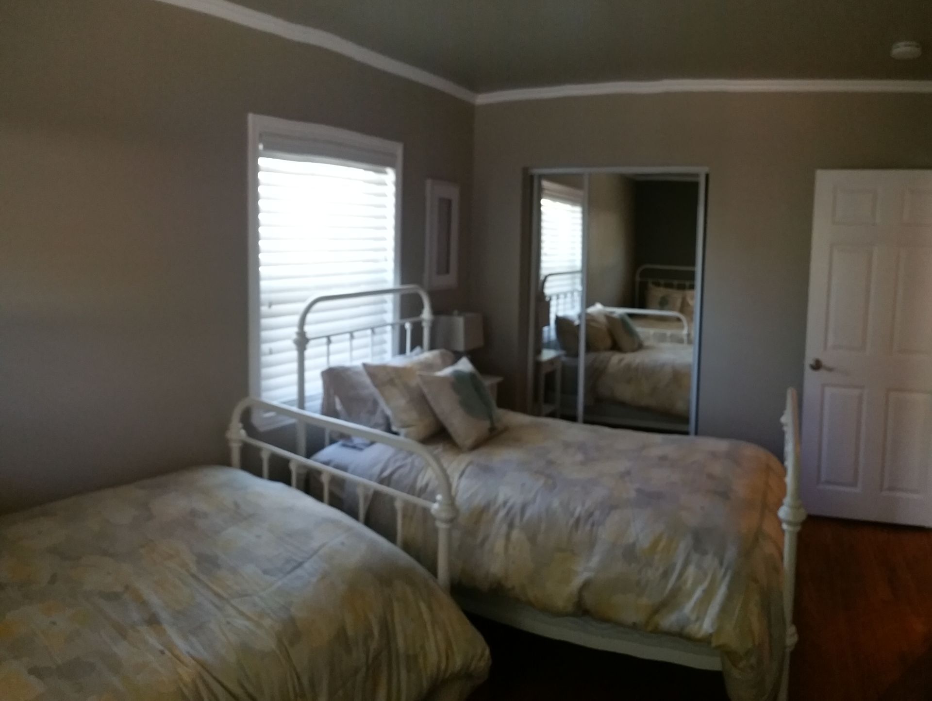 Bedroom with two single beds, mirrored closet doors, and a window with blinds.